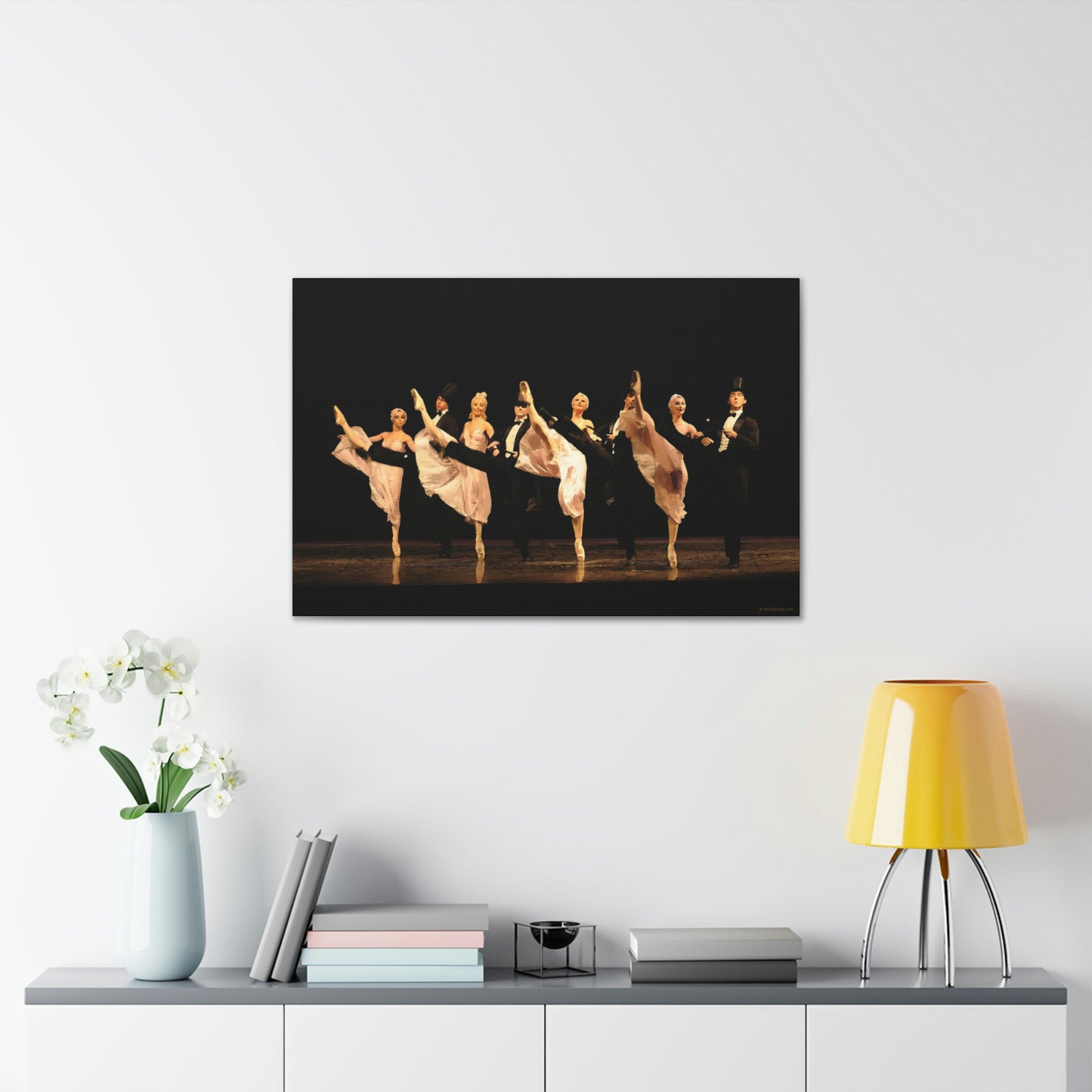 Artwork on a white wall over a desk of a kick line comprised of male and female dancers. Females are in white and the males are in tuxedos with top hats