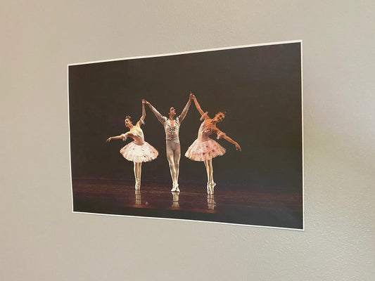 photo of a poster of 3 ballet dancers, 1 male, 2 female, performing on stage on a dark backdrop