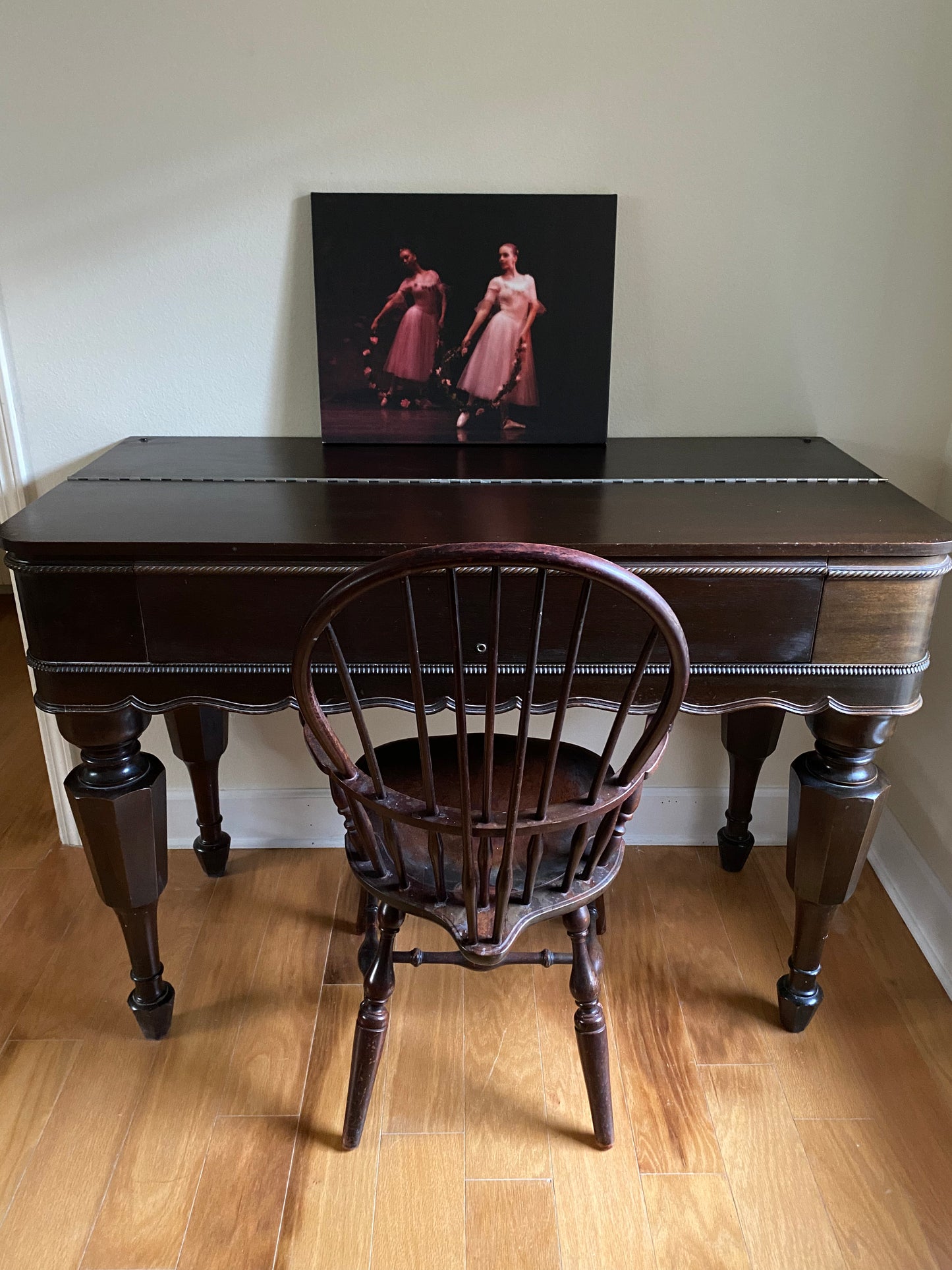 a photo of a painting sitting on a desk of two ballerinas posing on a dark backdrop wearing pink and holding pink rose wreathes
