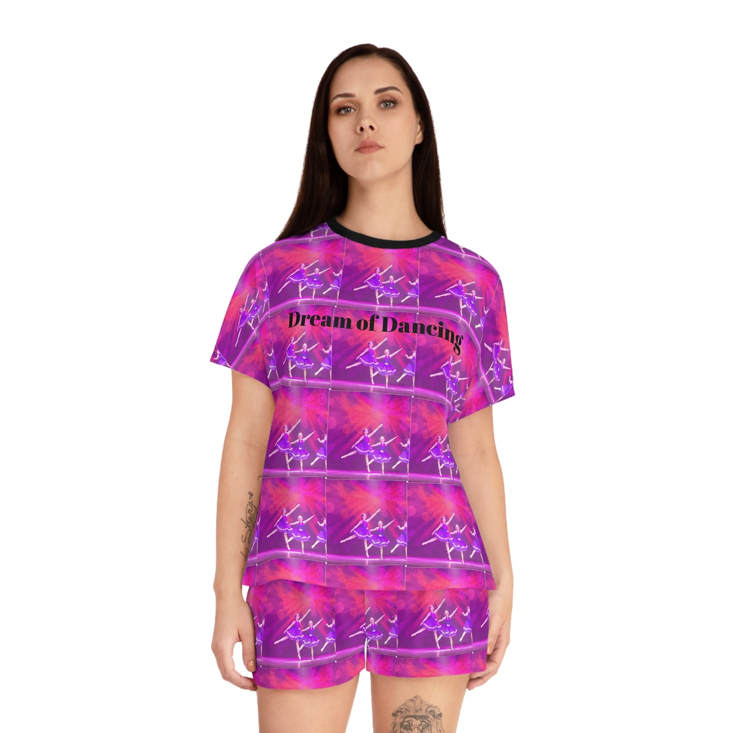 front view of a model wearing a short pajama set with black ribbed neck and Dream of Dancing written in black on a pink and purple ballerina print