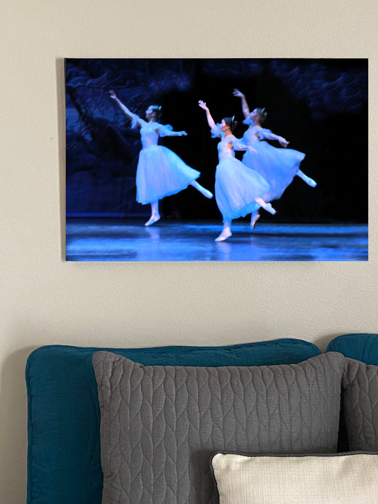 a photo of a painting in a home setting of three ballerinas performing on a stage dressed in white casting hues of blue