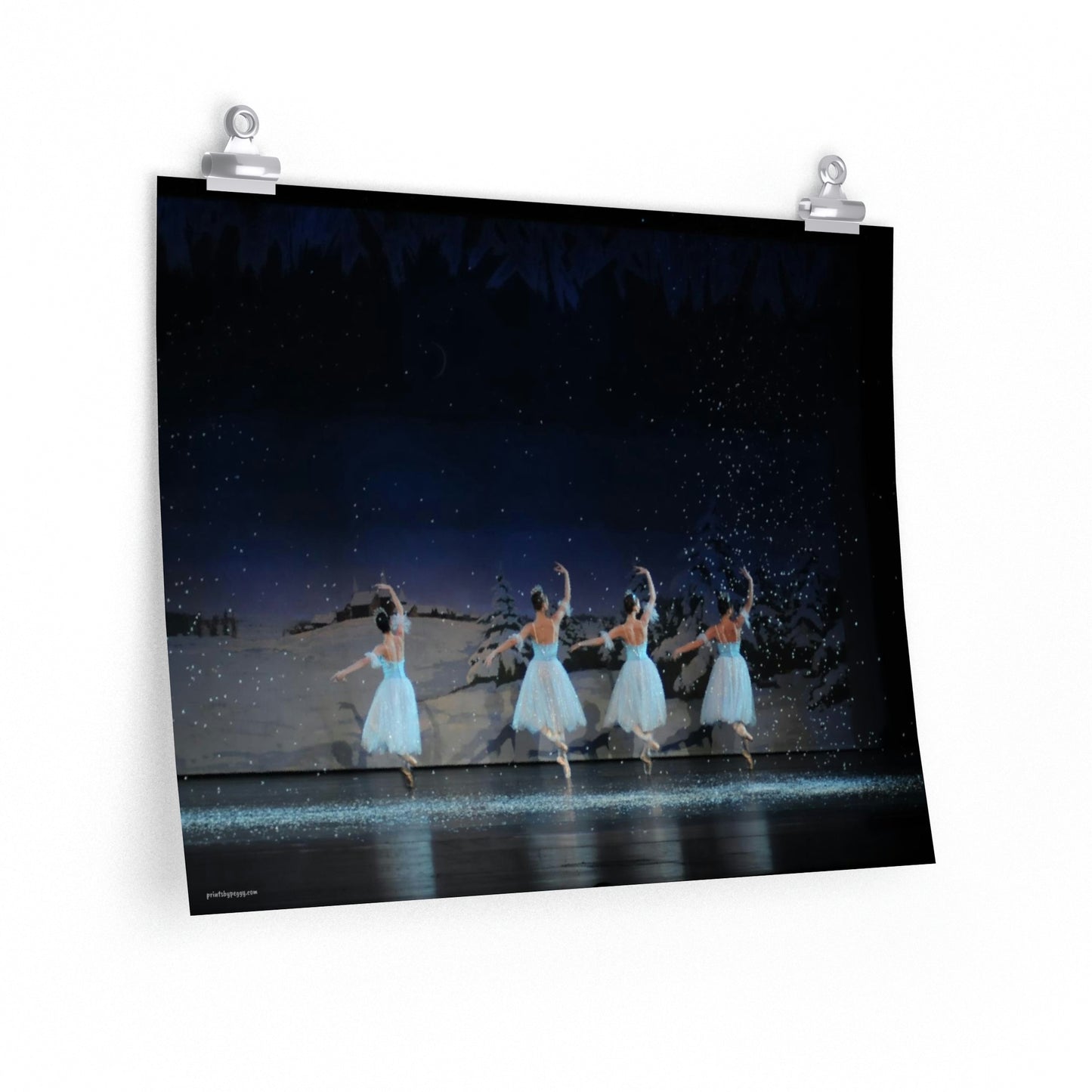 four ballet dancers dressed in blue with snow falling in a winter scene.