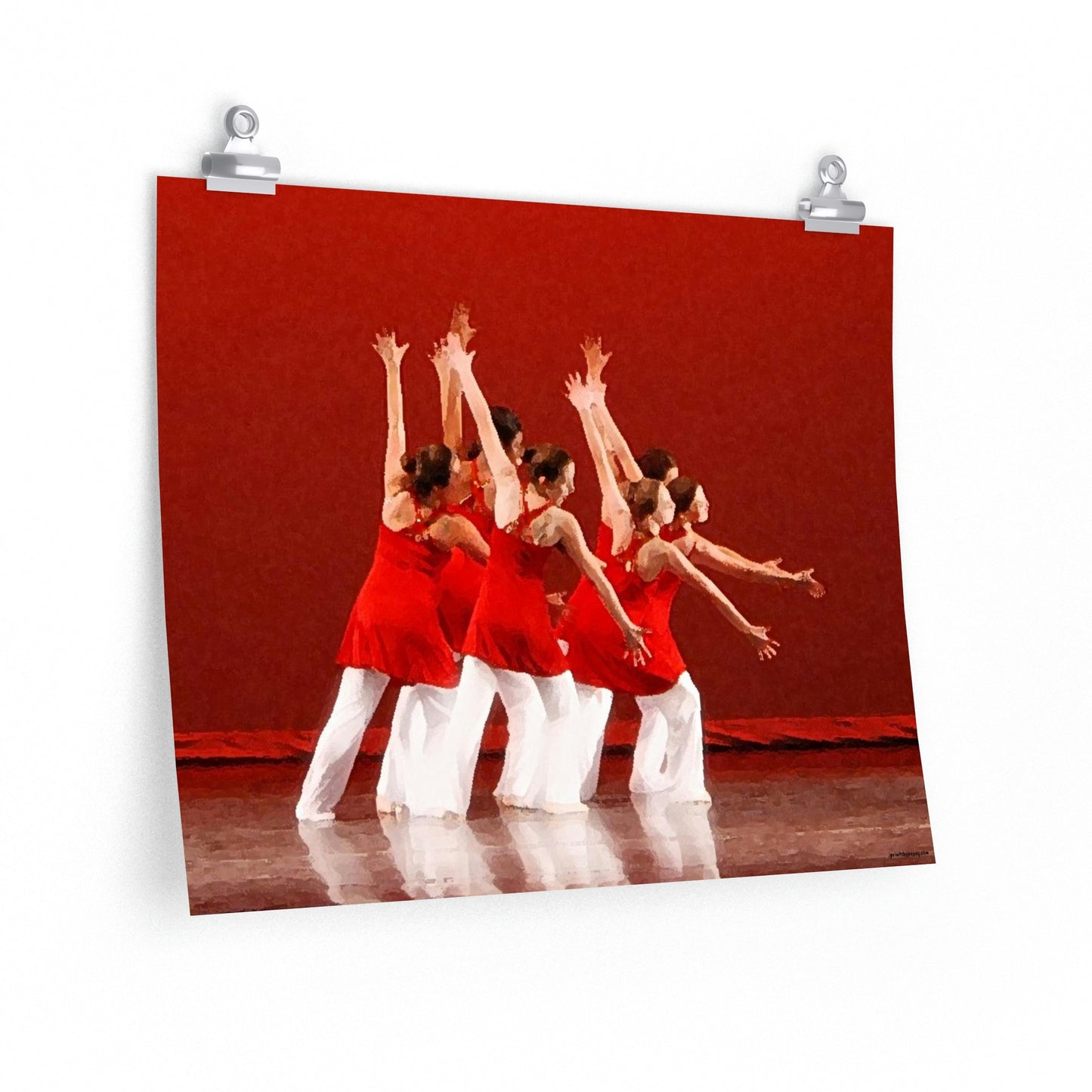 Poster hanging on a wall of seven modern dancers pictured from the side with both hands outstretched wearing red and white costumes on stage with a red back drop