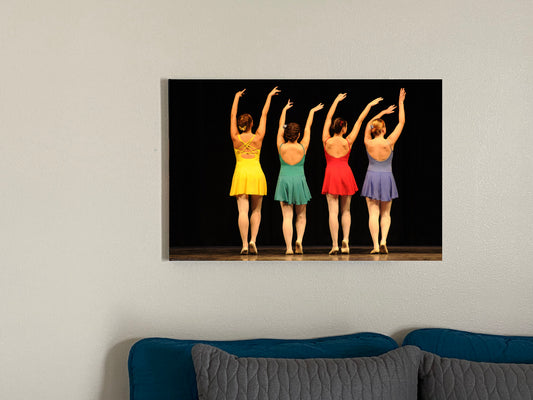 Art image hanging on the wall in a home setting of a painting of four modern dancers from the rear on stage in bright costumes