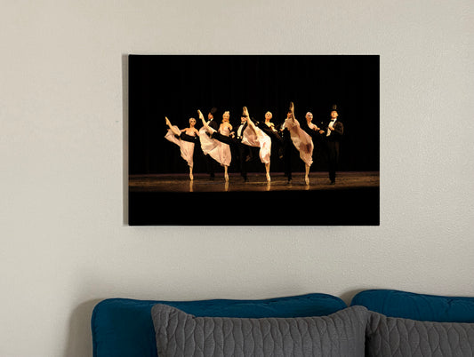 A kick line comprised of male and female dancers. Females are in white and the males are in tuxedos with top hats