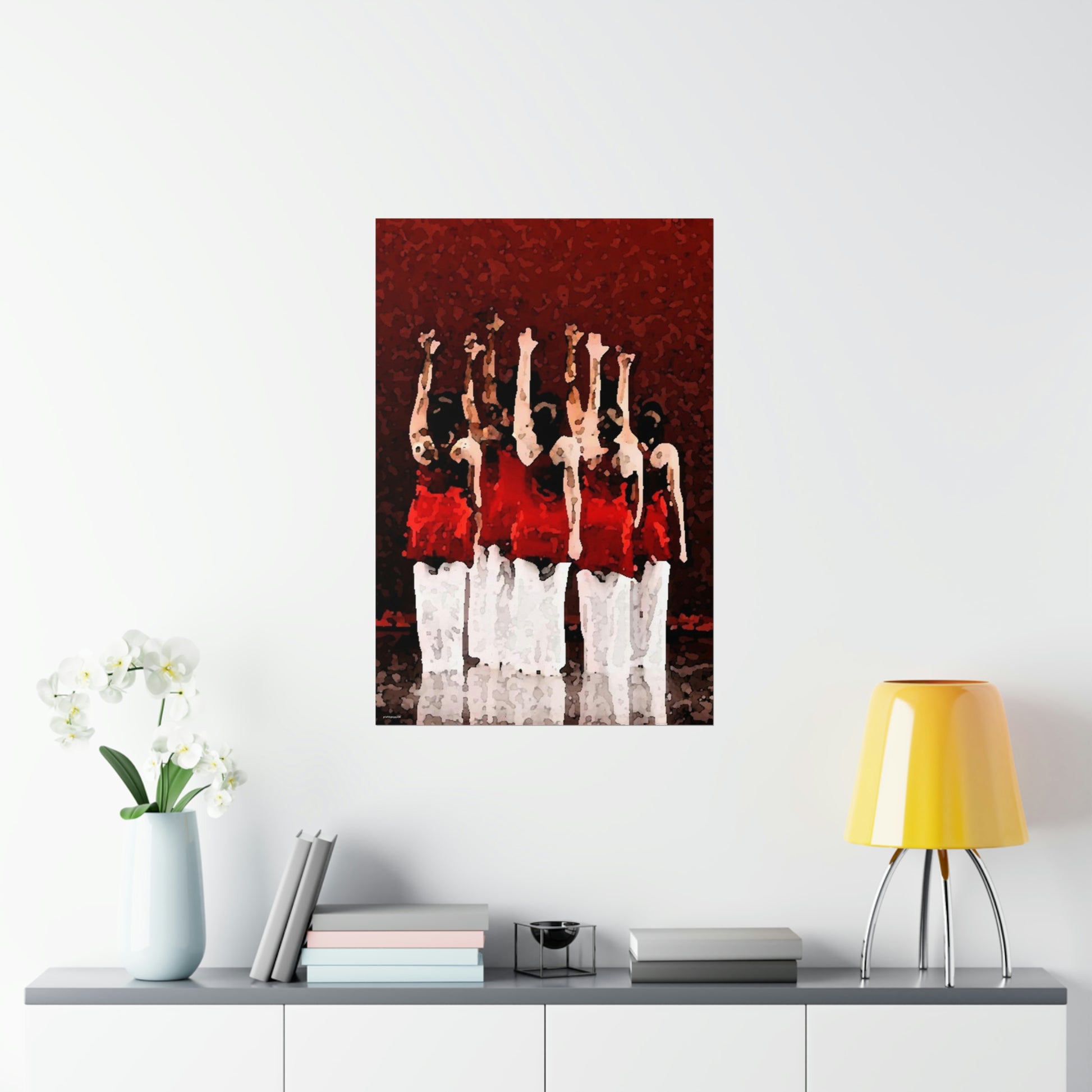 Poster hanging on a wall over a desk of seven modern dancers pictured from the rear with one hand outstretched wearing red and white costumes on stage with a red back drop