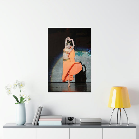 Poster hanging on a white wall of a dancer in orange belly dancer costume performing on stage