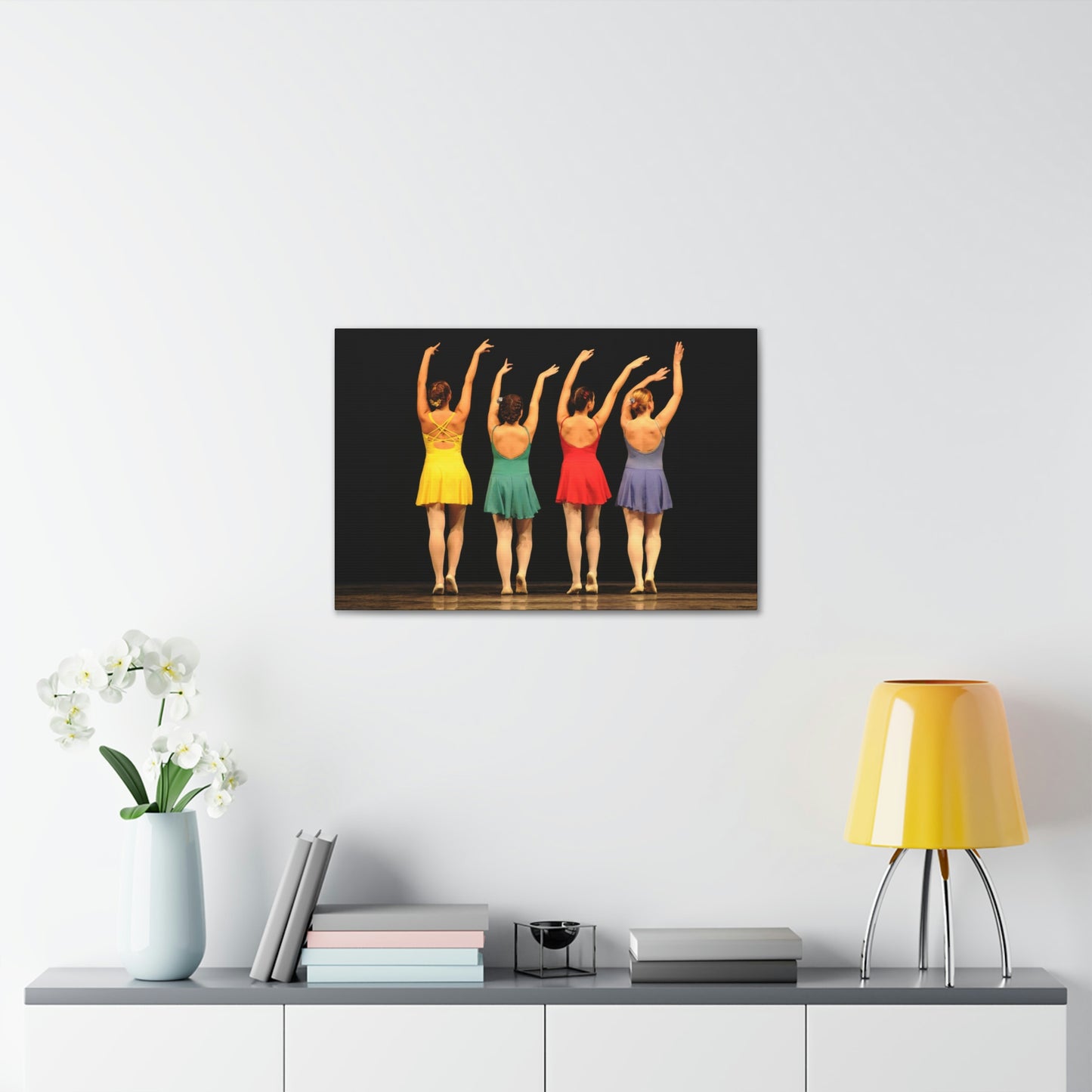 Art image hanging on the wall in a home setting of a painting of four modern dancers from the rear on stage in bright costumes