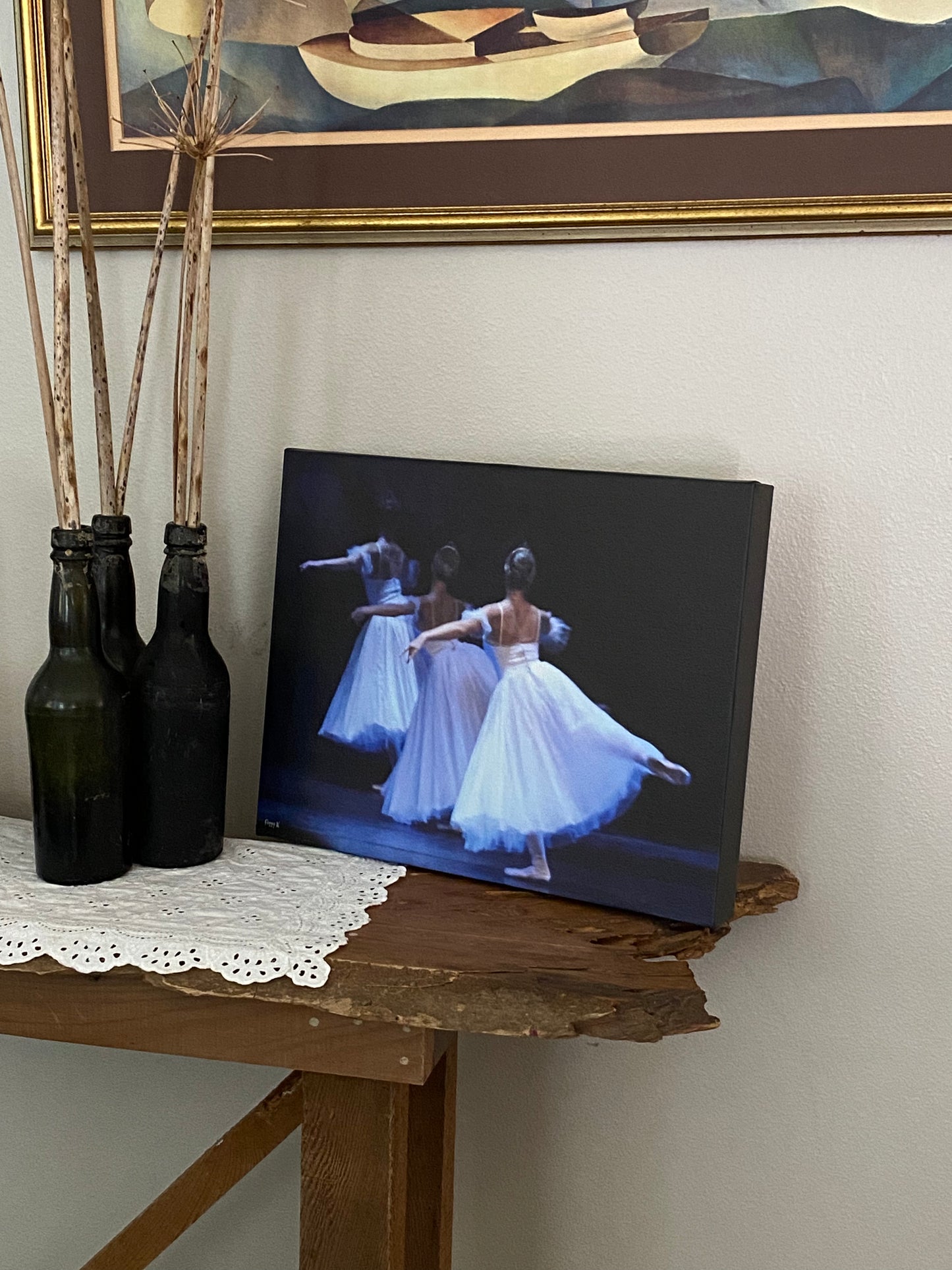 a photo of a painting placed on a table in a home decor setting of beautiful ballerinas performing on a stage with a dark backdrop