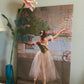 A photo of a painting of a ballerina in white gracefully posed on stage with a colorful backdrop or background