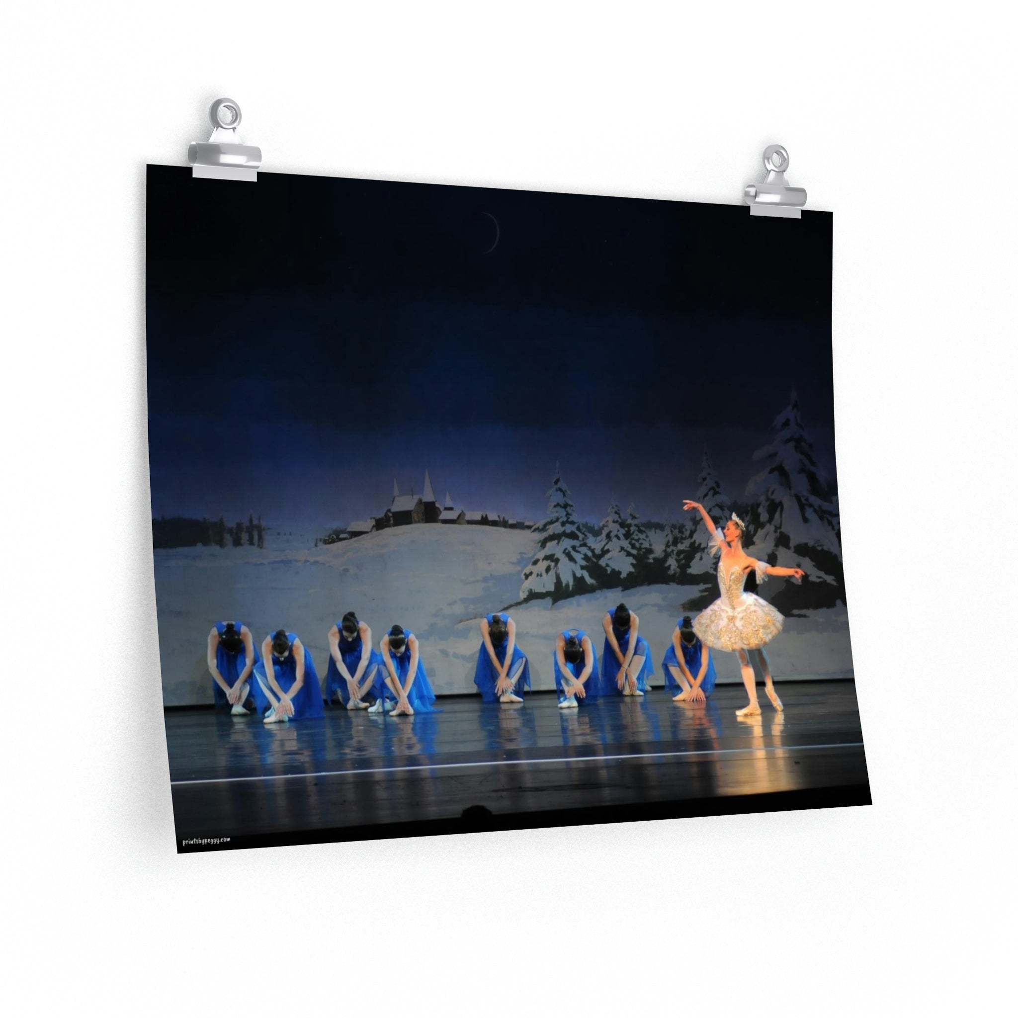 Prima ballerina performing on stage with 8 girls dressed in bright blue and a winter scene backdrop