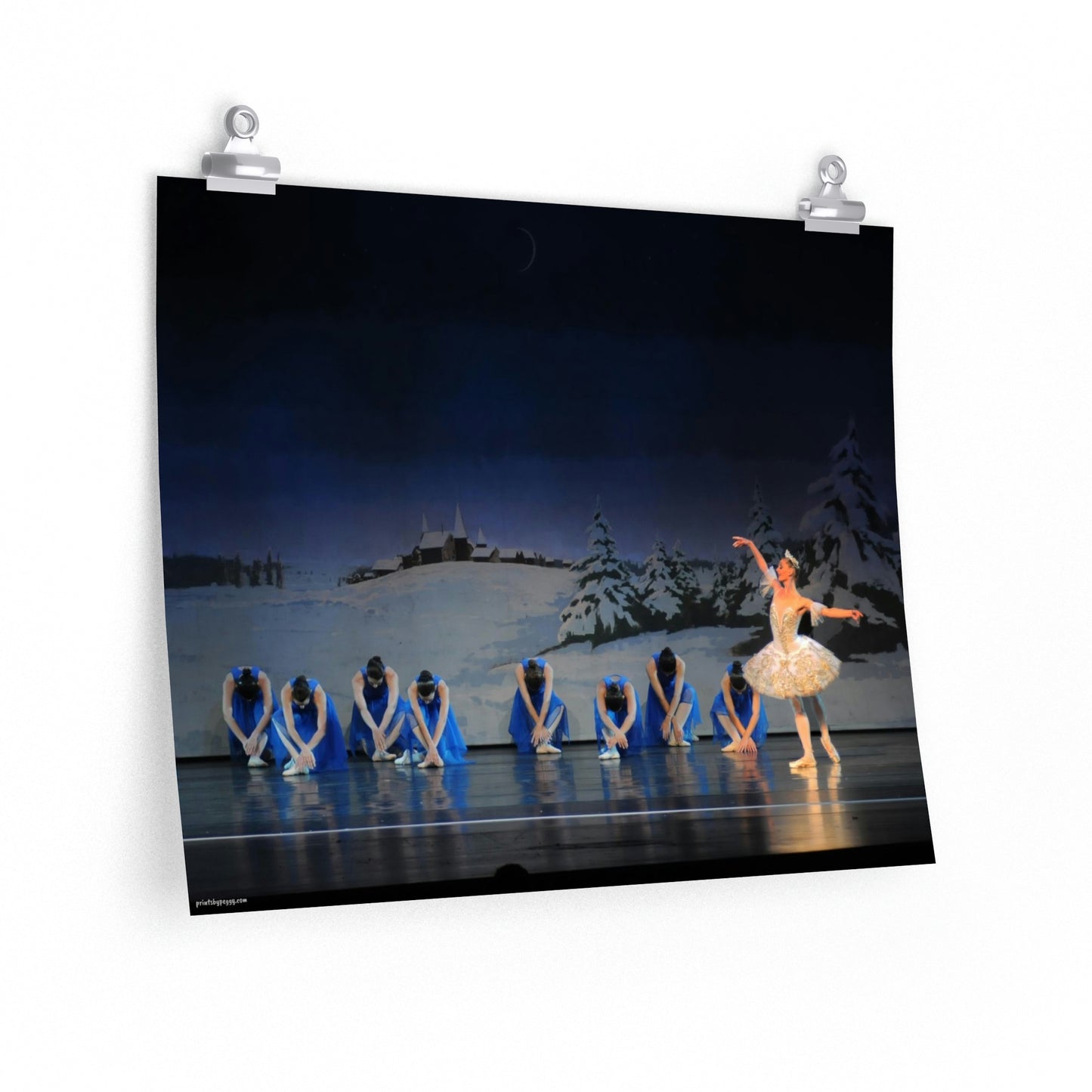 Prima ballerina performing on stage with 8 girls dressed in bright blue and a winter scene backdrop