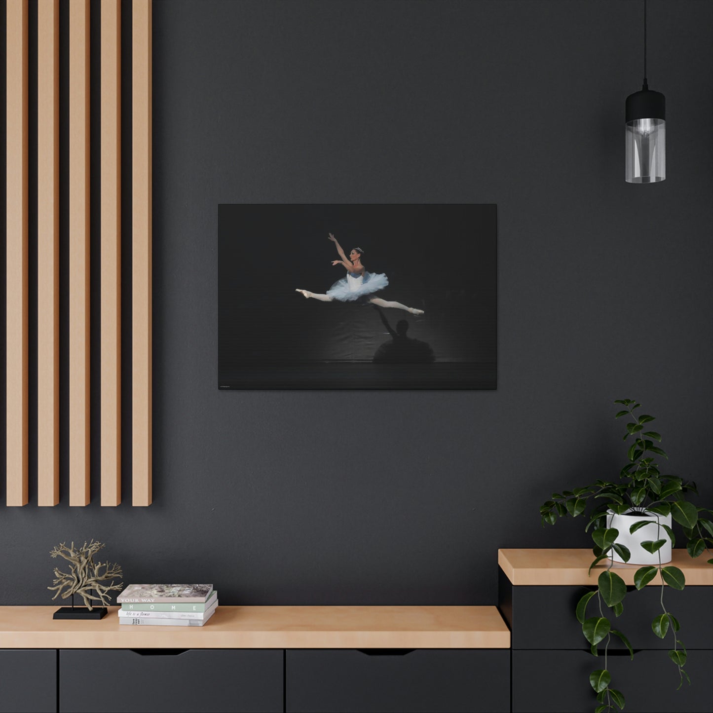 Canvas print of artwork hanging on a dark wall in a home setting of a Ballerina in a white tutu performing a mid-air leap. Light is casting her shadow on a black backdrop.