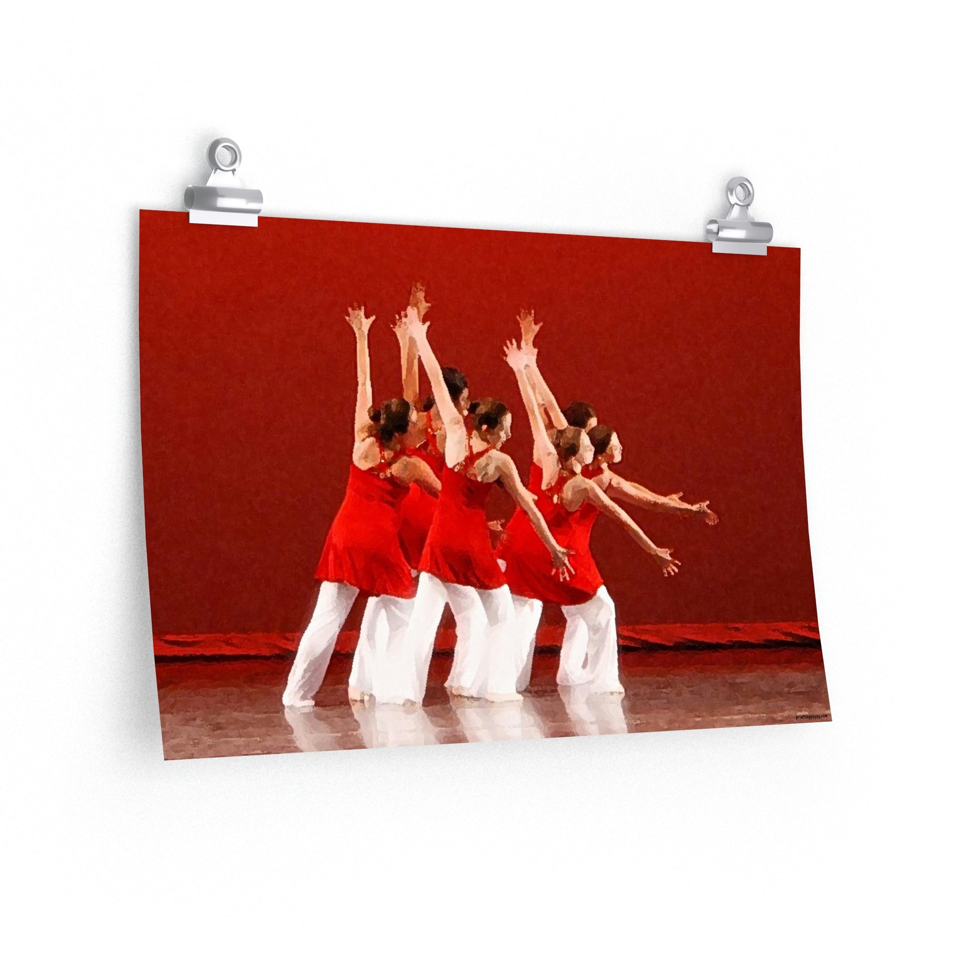 Poster hanging on a wall of seven modern dancers pictured from the side with both hands outstretched wearing red and white costumes on stage with a red back drop